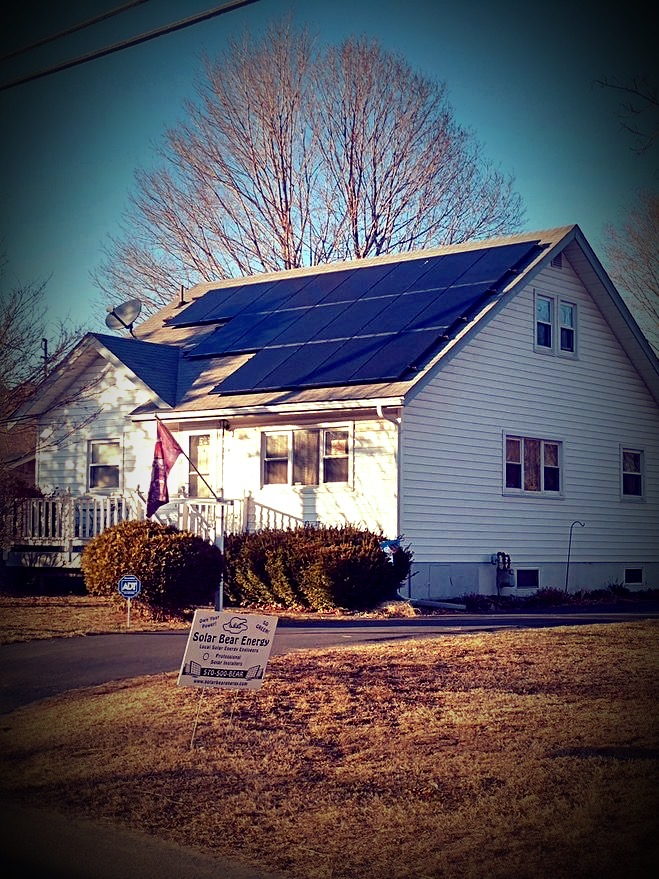 Completed black solar array on a white two-story home with a Solar Bear Energy yard sign out front