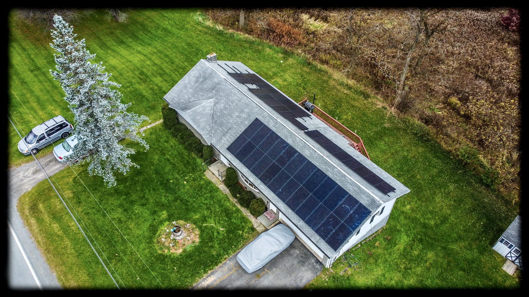 Aerial view of a white ranch home in the Tri-State area with black solar modules on both roof planes and utility lines running along the road